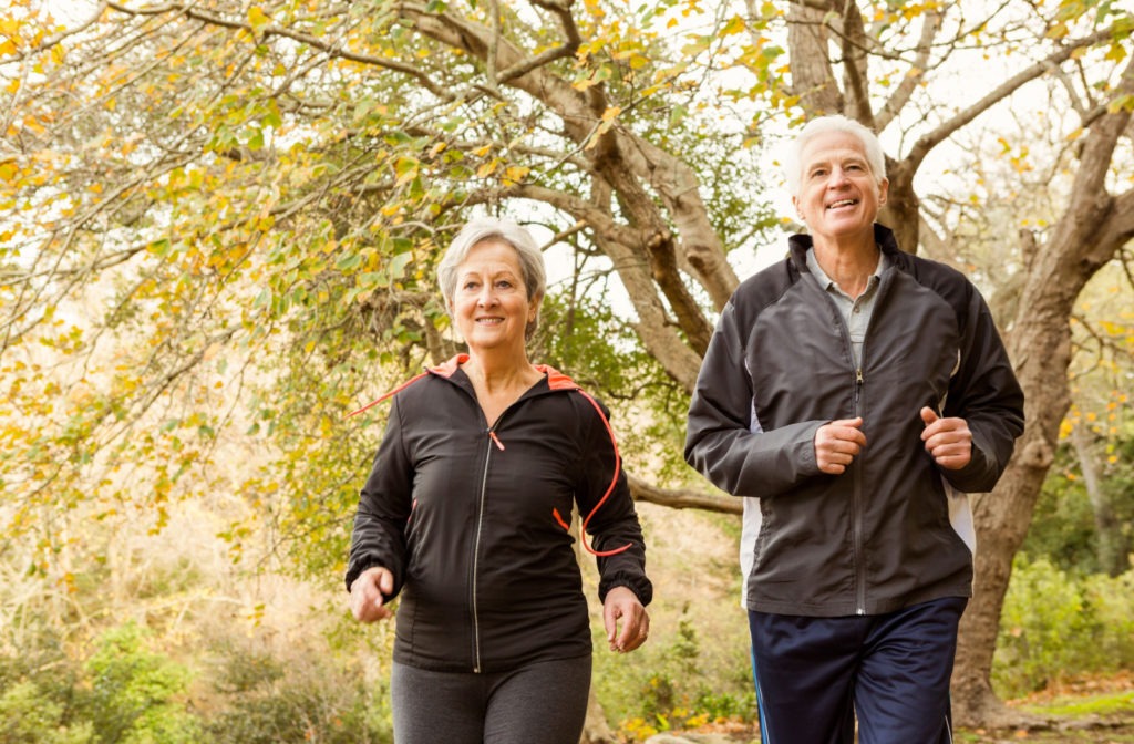 A senior man and a woman smiling while jogging outdoors.