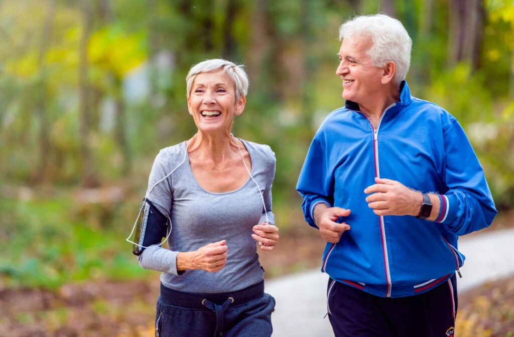 A senior man and a woman smiling while jogging outdoors.