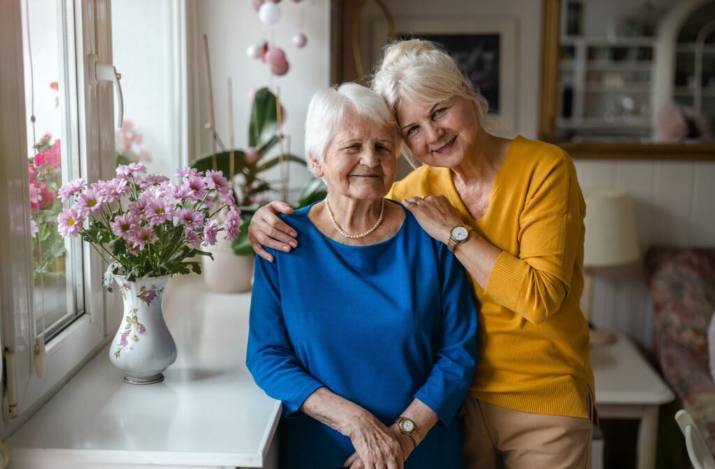 A senior resident smiles with their supportive child in a cozy home setting with a vase of flowers on a nearby table.