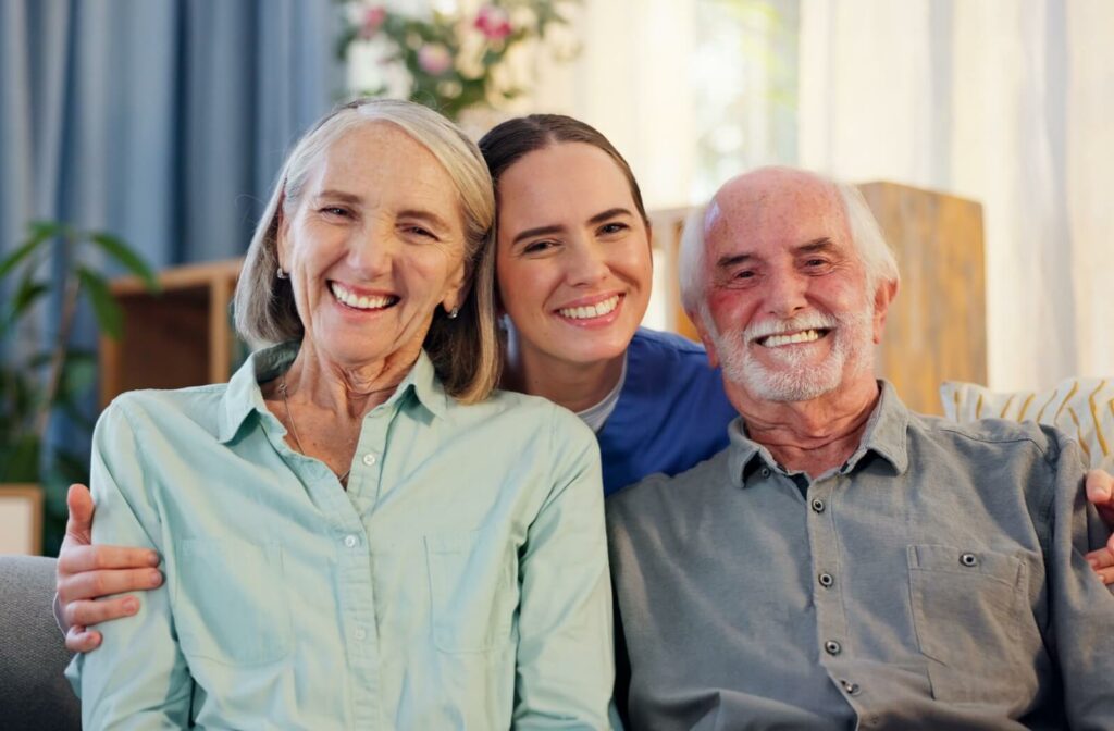 A nurse smiles in between a smiling older couple, happy to have moved into assisted living