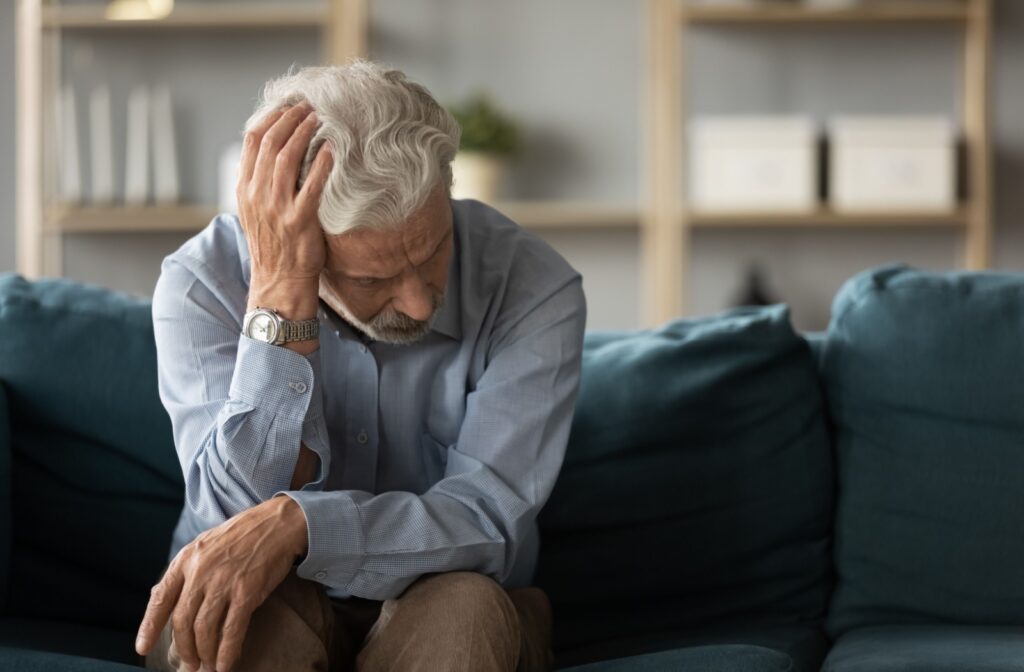 An older adult scratching their head while sitting on their couch and trying to remember something.