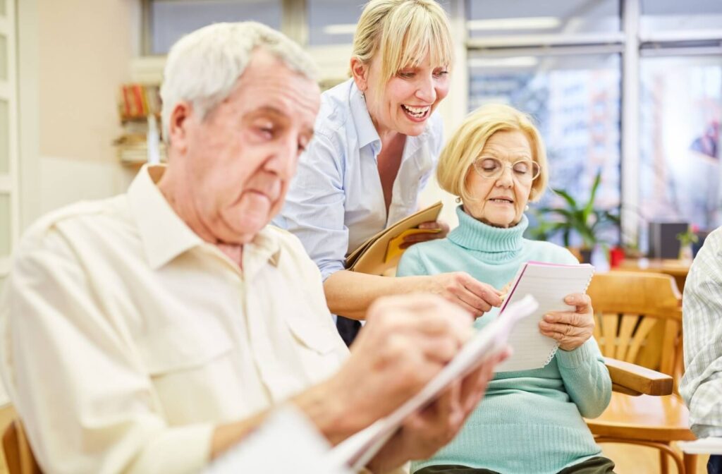 A memory care staff member engaging with two residents working on a written cognitive exercise.